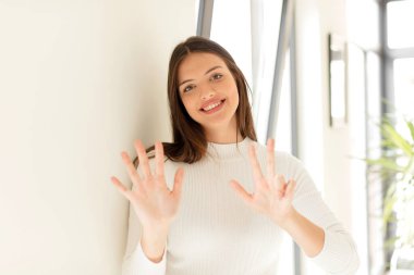 Güzel bir kadın gülümsüyor ve arkadaş canlısı görünüyor, 8 ya da 8 numarayı gösteriyor, elleri önde, geriye doğru sayıyor.