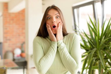 Güzel kadın şok olmuş ve korkmuş hissediyor, ağzı açık ve elleri yanaklarında korkmuş görünüyor.