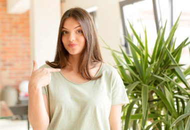 Güzel bir kadın gururlu, kendinden emin ve mutlu görünüyor, gülümsüyor ve kendini işaret ediyor veya bir numara işareti yapıyor.