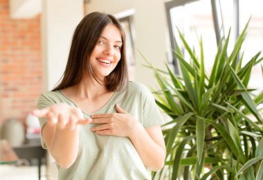 Güzel bir kadın mutlu ve aşık, bir eli kalbinin yanında, diğer eli önde uzanmış gülümsüyor.