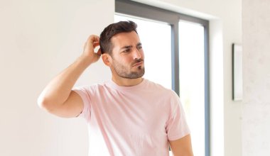 Yakışıklı adam şaşkın ve şaşkın hissediyor, başını kaşıyor ve yana bakıyor.