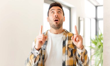 Yakışıklı bir adam şaşırmış ve ağzı açık bir şekilde şaşkın ve şaşkın bir bakışla yukarıya bakıyor.