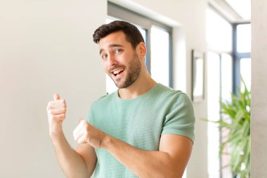 Yakışıklı adam neşeyle gülümsüyor ve tesadüfen fotokopi alanını işaret ediyor, mutlu ve tatmin olmuş hissediyor.