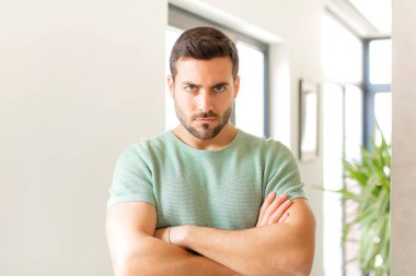 Yakışıklı adam üzgün ve hayal kırıklığına uğramış, ciddi görünüyor, sinirlenmiş ve kollarını kavuşturmuş.