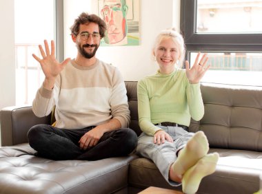 Genç çift gülümsüyor ve dost canlısı görünüyor, 5 ya da 5 numarayı gösteriyor, elleri önde, geriye doğru sayıyor.