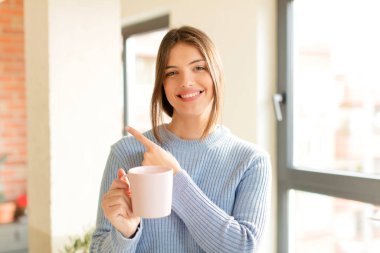 Güzel bir kadın neşeyle gülümsüyor, mutlu hissediyor ve kenarı ve yukarıyı işaret ediyor, fotokopi uzayındaki nesneleri gösteriyor.