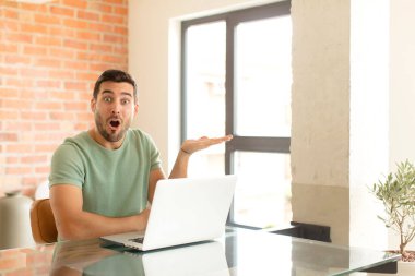 Yakışıklı adam şaşırmış ve şoka uğramış görünüyor, çenesi düşmüş, bir objeyi elinde açık bir elle tutuyor.