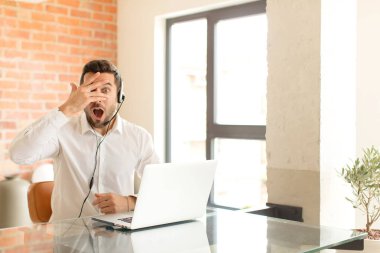 Yakışıklı pazarlamacı şok olmuş, korkmuş ya da korkmuş görünüyor. Yüzü elle kaplanmış ve parmaklarının arasından gizlice bakıyor.