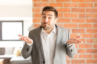 Yakışıklı iş adamı şaşkın ve şaşkın hissediyor, şüpheci, farklı seçenekleri tartıyor veya komik bir ifadeyle seçiyor.