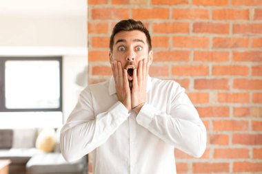 Yakışıklı iş adamı şok olmuş ve korkmuş hissediyor, ağzı açık ve elleri yanaklarında korkmuş görünüyor.