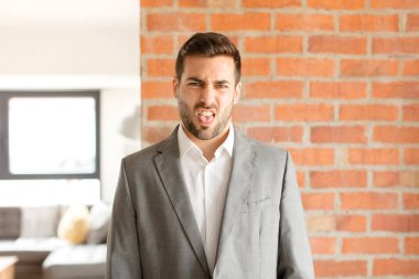 Yakışıklı iş adamı iğrenmiş ve rahatsız olmuş hissediyor, dilini dışarı çıkarıyor, iğrenç ve iğrenç bir şeyden hoşlanmıyor.