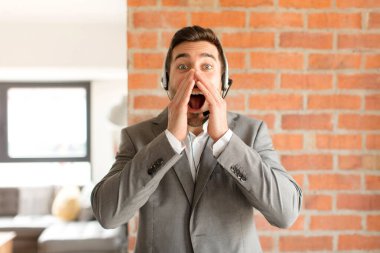 Yakışıklı pazarlamacı mutlu, heyecanlı ve pozitif hissediyor. Elleri ağızda, bağırıyor.