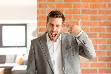 Yakışıklı iş adamı mutsuz ve stresli görünüyor, intihar jesti elle silah işareti yapıyor, kafasını işaret ediyor.