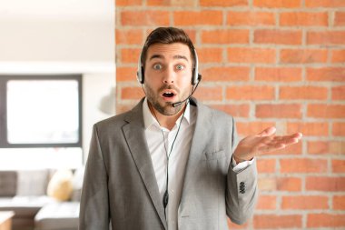 Yakışıklı tele-pazarlamacı şaşırmış ve şok olmuş görünüyor, çenesi düşmüş, bir objeyi elinde açık bir elle tutuyor.