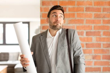 Yakışıklı mimar omuz silkiyor, kafası karışık ve kararsız, kolları bağlı ve şaşkın görünüyor.