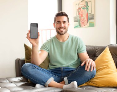 Yakışıklı adam mutlu bir şekilde gülümsüyor, eli kalçasında ve kendinden emin, olumlu, gururlu ve arkadaş canlısı.