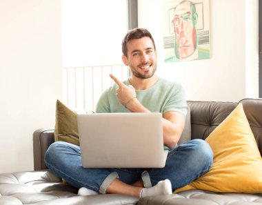 Yakışıklı adam neşeyle gülümsüyor, mutlu hissediyor ve yan ve yukarı doğru işaret ediyor, fotokopi uzayındaki nesneleri gösteriyor.