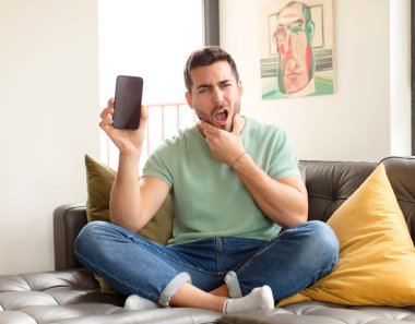 Ağzı ve gözleri açık, eli çenesinde olan yakışıklı bir adam, nahoş bir şekilde şokta, ne ya da vay canına diyor.