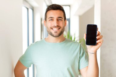 Yakışıklı adam mutlu bir şekilde gülümsüyor, eli kalçasında ve kendinden emin, olumlu, gururlu ve arkadaş canlısı.