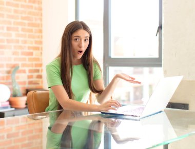 Güzel bir kadın şaşırmış ve şoka uğramış görünüyor, çenesi düşmüş, elinde açık bir elle bir nesne tutuyor.