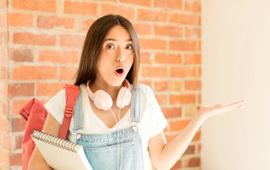 Şaşırmış ve şoke olmuş bir halde, çenesi düşmüş bir objeyi elinde açık bir elle tutarken.