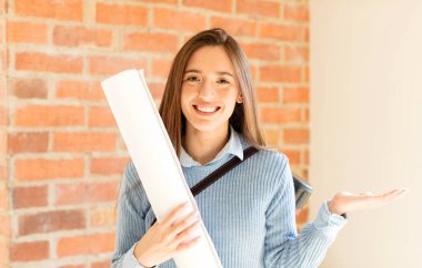 Güzel mimar mutlu bir şekilde gülümsüyor, mutlu hissediyor ve bir konsepti fotokopi uzayında avuç içiyle gösteriyor.