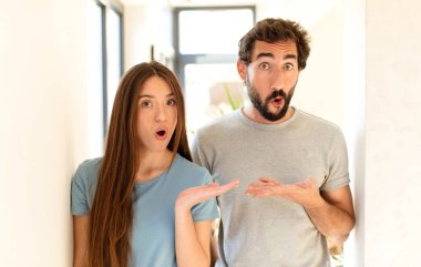 Genç çift şaşırmış ve şoka uğramış görünüyor, çeneleri düşmüş, ellerinde açık bir elle bir nesne tutuyorlar.