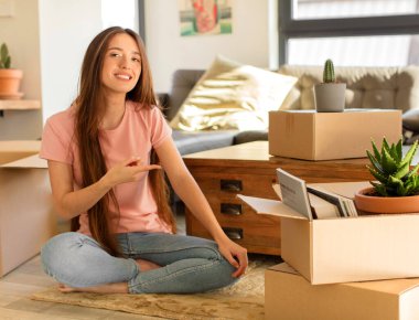 Güzel bir kadın neşeyle gülümsüyor, mutlu hissediyor ve kenarı ve yukarıyı işaret ediyor, fotokopi uzayındaki nesneleri gösteriyor.