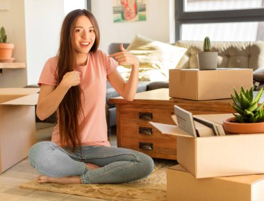 Güzel bir kadın mutlu, şaşırmış ve gururlu hissediyor, heyecanlı ve şaşkın bir bakışla kendini işaret ediyor.