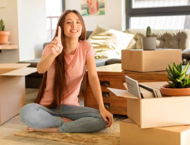 Güzel bir kadın gülümsüyor ve arkadaş canlısı görünüyor. Bir numarayı gösteriyor ya da ilk eli önde, geri sayıyor.