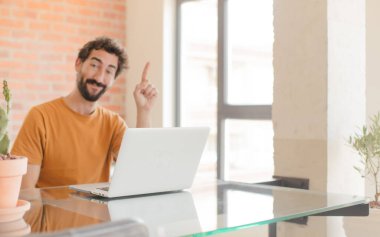 Genç sakallı adam gülümsüyor ve arkadaş canlısı görünüyor. Bir numara ya da ilk eli önde, geriye doğru sayıyor ve dizüstü bilgisayarla çalışıyor.