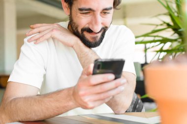 Evde akıllı telefonu olan sakallı genç bir adam.