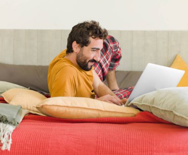 Yatakta dizüstü bilgisayarlı genç sakallı bir adam.