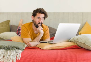 Yatakta dizüstü bilgisayarlı genç sakallı bir adam.