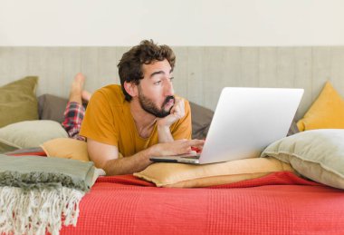 Yatakta dizüstü bilgisayarlı genç sakallı bir adam.