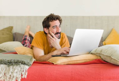 Yatakta dizüstü bilgisayarlı genç sakallı bir adam.