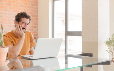 Evde dizüstü bilgisayarla çalışan sakallı genç bir adam.