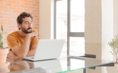 Evde dizüstü bilgisayarla çalışan sakallı genç bir adam.