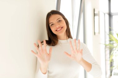 Güzel bir kadın gülümsüyor ve arkadaş canlısı görünüyor. 9 ya da 9 numarayı gösteriyor. Elleri önde ve geri sayıyor.