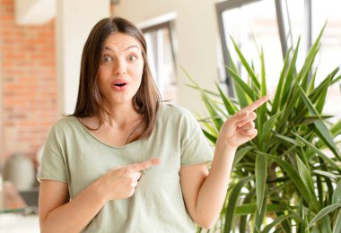 Güzel bir kadın mutlu ve şaşırmış hissediyor, şok olmuş bir ifadeyle gülümsüyor ve bir tarafı işaret ediyor.