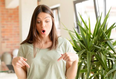 Güzel bir kadın şoke olmuş, ağzı açık ve şaşırmış, inançsızlık ve şaşkınlık içinde bakıyor ve onu işaret ediyor.