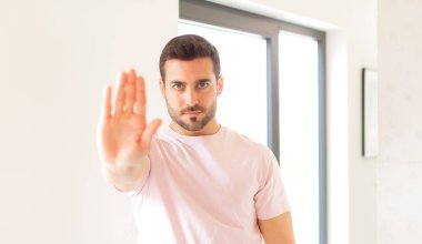 Yakışıklı adam ciddi, sert, hoşnutsuz ve kızgın görünüyor. Avuç içini açıp jesti durduruyor.