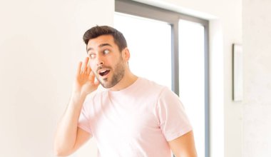 Yakışıklı adam gülümsüyor, tuhaf bir şekilde yan tarafa bakıyor, dedikoduları dinlemeye ya da bir sırrı duymaya çalışıyor.