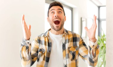 Yakışıklı adam kendini mutlu, şaşkın, şanslı ve şaşırmış hissediyor. Zaferi kutlarken iki eli havada.
