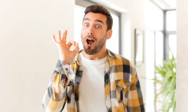 Yakışıklı adam kendini başarılı ve tatmin olmuş hissediyor, ağzı açık gülümsüyor, elle işaret veriyor.