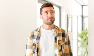 Yakışıklı adam şaşkın ve şaşkın görünüyor, merak ediyor veya bir sorunu çözmeye çalışıyor veya düşünüyor.