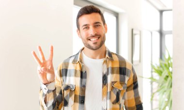 Yakışıklı adam gülümsüyor ve arkadaş canlısı görünüyor. Üç ya da üç numarayı gösteriyor. Elleri önde, geriye doğru sayıyor.