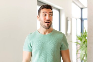 Yakışıklı adam şaşkın, mutlu, şaşkın ve şaşırmış hissediyor, ağzı açık bir şekilde yana bakıyor.