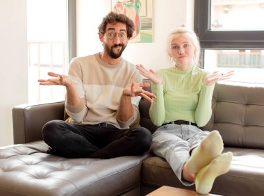 Genç çift şaşkın ve şaşkın hissediyor, şüpheci, farklı seçenekleri tartıyor veya komik bir ifadeyle seçiyor.