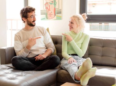 Genç çift neşeyle gülümsüyor, mutlu hissediyorlar ve kenarları ve yukarıyı gösteriyorlar, fotokopi alanında nesneler gösteriyorlar.